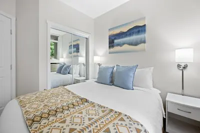 a white bedroom with a large bed with blue pillows at Alpenglow Lodge West Coast Wonder by MVA in Whistler