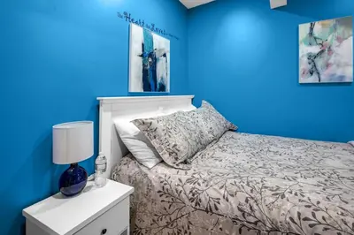 a blue bedroom with a bed and a nightstand with a lamp at 52-3 Bed Suite On Lake Central Ac By Airport in Calgary