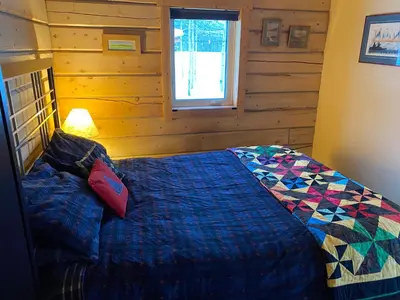 a bedroom with a bed with a blue comforter and a window at Oma's and Opa's Northern Lights Viewing Cabin in Whitehorse
