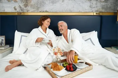 a man and a woman sitting in bed with a tray of food at AZUR Legacy Collection Hotel in Vancouver