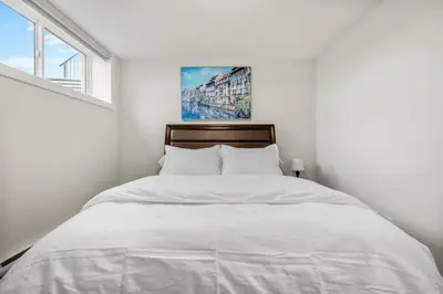 a white bedroom with a large bed with white sheets at Rockland Oasis: 1BR + Parking in Calgary