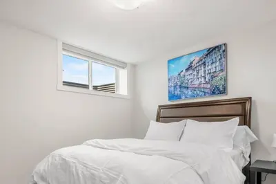 a bedroom with a bed with white sheets and two windows at Rockland Oasis: 1BR + Parking in Calgary