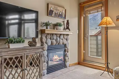 a stone fireplace in a living room with a window at Top Floor Wolf - Best Views With Pool and Hot tub in Canmore