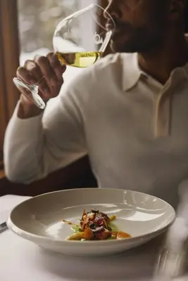 a man drinking a glass of wine with a plate of food at Post Hotel & Spa in Lake Louise