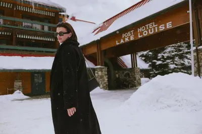 a woman standing in the snow in front of a lodge at Post Hotel & Spa in Lake Louise