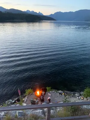 a group of people sitting around a fire next to a lake at Earls Cove Orca View in Egmont