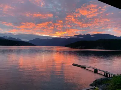 a sunset on a lake with a dock in the water at Earls Cove Orca View in Egmont