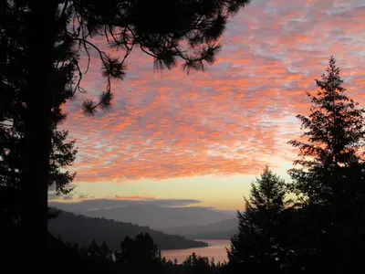 a sunset with a view of a lake and trees at Okanagan Lake Sunrise BB in Vernon