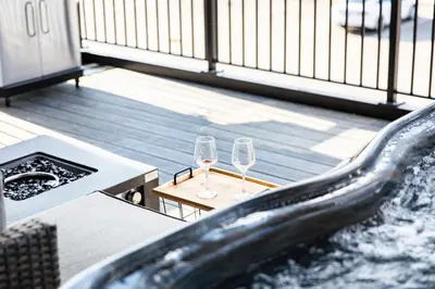 two wine glasses on a balcony with a hot tub at The Shred Shack - Stylish Revelstoke Condo in Revelstoke