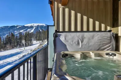 a hot tub on a balcony with a snow covered mountain at Altitude #36 condo in Sun Peaks
