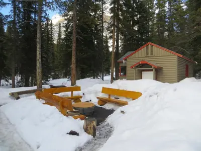 a cabin in the snow with benches in front of it at HI Mosquito Creek - Wilderness Hostel in Lake Louise