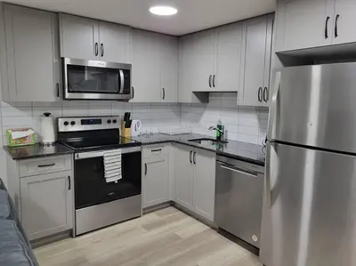 a kitchen with white cabinets and a stainless steel refrigerator at Serene Haven - 1 bedroom apartment. in Calgary