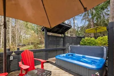 a hot tub on a deck with a red chair and an umbrella at Salt Spring Carriage House B&B in Ganges