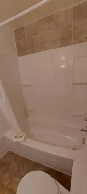 a white bathroom with a toilet and a tub at Granby River Inn & Suites in Grand Forks