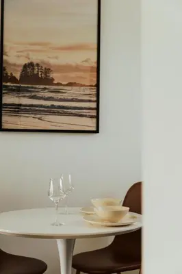 a white table with two wine glasses and a picture at Ucluelet Wildwood Inn in Ucluelet