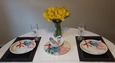 a table with two plates and a vase with yellow flowers at Comfy KING Bed, Large private Basement Suite, Smart TV in Penticton- city of PEACHES AND BEACHES in Penticton