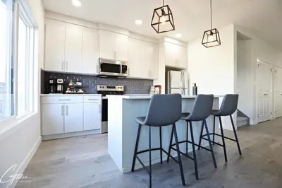 a kitchen with white cabinets and a bar with stools at Beautiful 3 King Beds,Garage,Airport,Disney+ in Edmonton