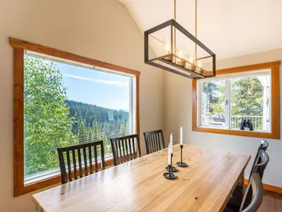a dining room with a wooden table and a large window at The Alpine I No Service Fee's I Ski-in Ski-Out I in Silver Star