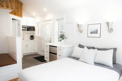 a white bedroom with a bed and a kitchen at Surfs Inn Guesthouse & Cottages in Ucluelet