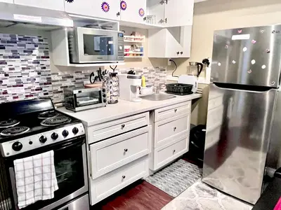 a kitchen with white cabinets and a stainless steel refrigerator at Cozy Walkout suite with King bed, Kitchen, Parking & Patio in Calgary