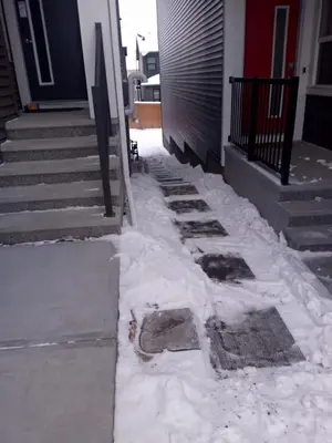 a sidewalk covered in snow next to a house at Cozy brand new 2 bedroom suite in Calgary in Calgary