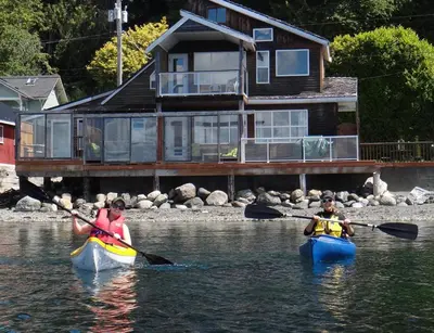 two people in kayaks in the water in front of a house at Orca Lodge in Sointula