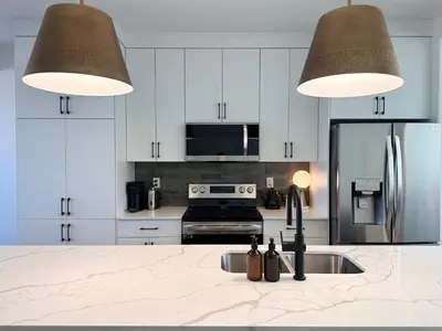 a kitchen with white cabinets and a sink and two lights at The Evergreen House in Red Deer