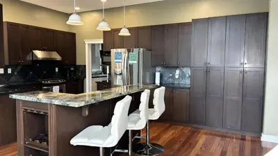 a kitchen with wooden cabinets and white stools at a counter at Metropolitan Dream Stay with Saltwater Pool and Hot Tub in Surrey