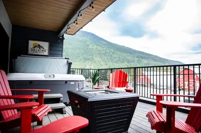 a porch with a grill and red chairs on a deck at Selkirk Staytion - Stylish Condo with Hot Tub in Revelstoke