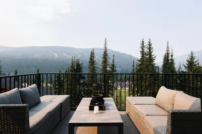 a balcony with couches and a table with a view at New! Luxury, Top Floor, Ski in/Ski Out, Private Hot Tub and Mountain Views in Sun Peaks