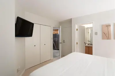 a white bedroom with a bed and a tv on a cabinet at Woodrun Lodge 216 | Renovated Ski-In Ski-Out Condo w/ Free Parking, Pool, Hot Tub, & Gym in Whistler