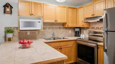 a kitchen with wooden cabinets and a sink and a microwave at Woodrun Lodge 214 | Ski-in-Ski-Out Condo, Heated Pool, Hot Tub, Gym in Whistler