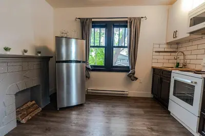 a kitchen with a stainless steel refrigerator in front of a fireplace at Historical Building 1br 1ba Walk To Rogers Place in Edmonton