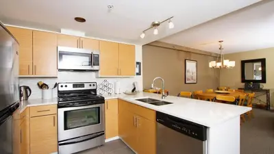 a kitchen with a stove and a sink and a table at Woodrun Lodge 211 | Ski-In Ski-Out Condo w/ Heated Pool, Hot Tub, Parking, & Gym in Whistler