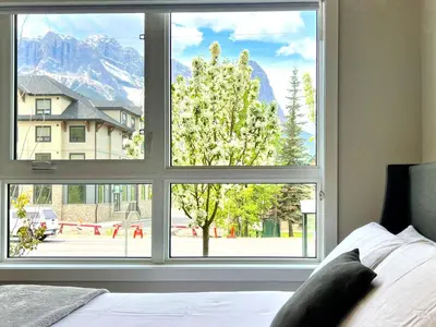a bedroom with a large window with a mountain view at Brand New 2BR Condo with Outdoor Swimming Pool and Hot Tub in Canmore