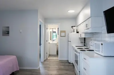 a white kitchen with white appliances and a hallway at Poplars Motel on the lake in Osoyoos