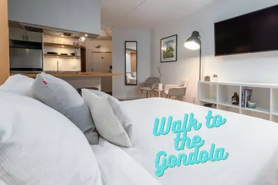 a bedroom with a white bed and a kitchen at Casa Creekside - Walk to Gondola, Shops, lakes! in Whistler