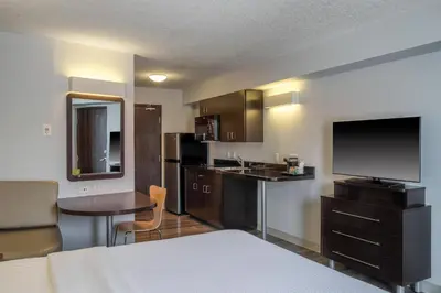 a room with a bed and a kitchen with a television at Motel 6 Airdrie in Airdrie
