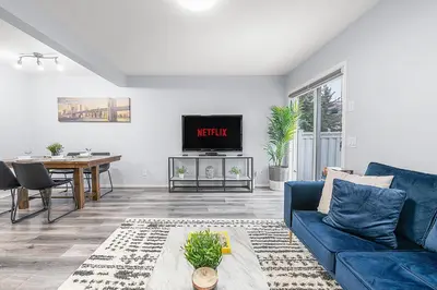 a living room with a blue couch and a table at Large Townhome Near Anthony Henday in Ellerslie with Driveway & Visitor Parking, King Bed, 4 Queen Beds, Fully Equipped Kitchen & More! in Edmonton