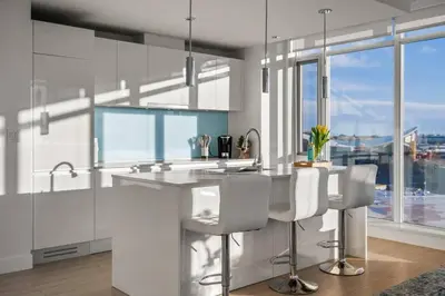 a kitchen with white cabinets and a counter with chairs at Luxury Apartment on the 9th Floor near Stampede, Complimentary Wine, 2 Car UG Parking in Calgary