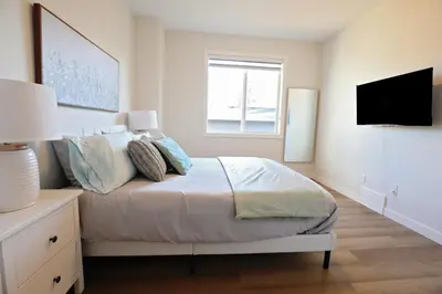 a white bedroom with a bed and a television at Central 5 Bedroom, AC, Rogers, Commonwealth, EXPO in Edmonton