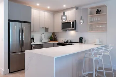 a kitchen with white cabinets and a refrigerator and stools at The Stoke Stopover - Revelstoke Condo with Hot Tub in Revelstoke