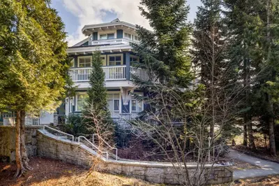 a large white house surrounded by trees at 2BR in Granite Court, Village Location, Gas Fireplace, Mudroom, Secure Parking in Whistler