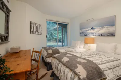 two beds in a room with a table and a desk at 3BR and Den in Gleneagle, Wood Burning Fireplace, Heated Flooring, Secure Parking in Whistler