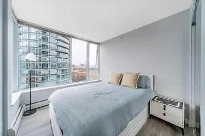 a white bedroom with a bed and a large window at Near BC Place & SkyTrain Access & Free Parking in Vancouver