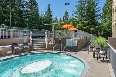 a swimming pool with chairs and an umbrella at Woodrun Lodge 414 | Cozy Ski-In Ski-Out Condo w/ Shared Hot Tub, Pool, Fireplace, & Parking in Whistler