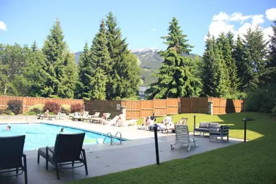 a swimming pool with chairs and people sitting around it at Cascade Lodge with front desk check in services, ski valet service, boot and glove dryer, 2 hot tubs, year round heated pool, gym, sauna, change rooms & showers, WIFI, cable TV in Whistler