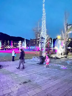 a woman and a child walking in a park with christmas lights at Cascade Lodge with front desk check in services, ski valet service, boot and glove dryer, 2 hot tubs, year round heated pool, gym, sauna, change rooms & showers, WIFI, cable TV in Whistler