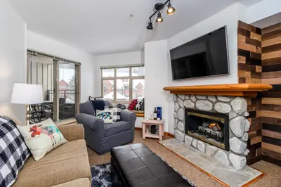 a living room with a fireplace with a tv above it at Creekside Slopeside 1BR with pool, hot tub, BBQ in Whistler