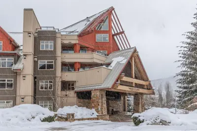 a large house in the snow with snow at Creekside Slopeside 1BR with pool, hot tub, BBQ in Whistler